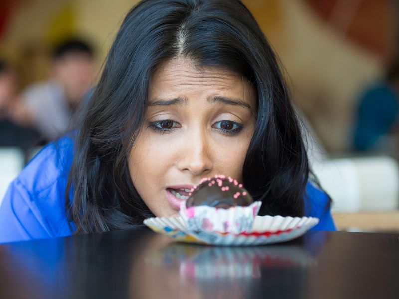 A woman wanting to eat a chocolate muffin to cope with stress of anxiety.