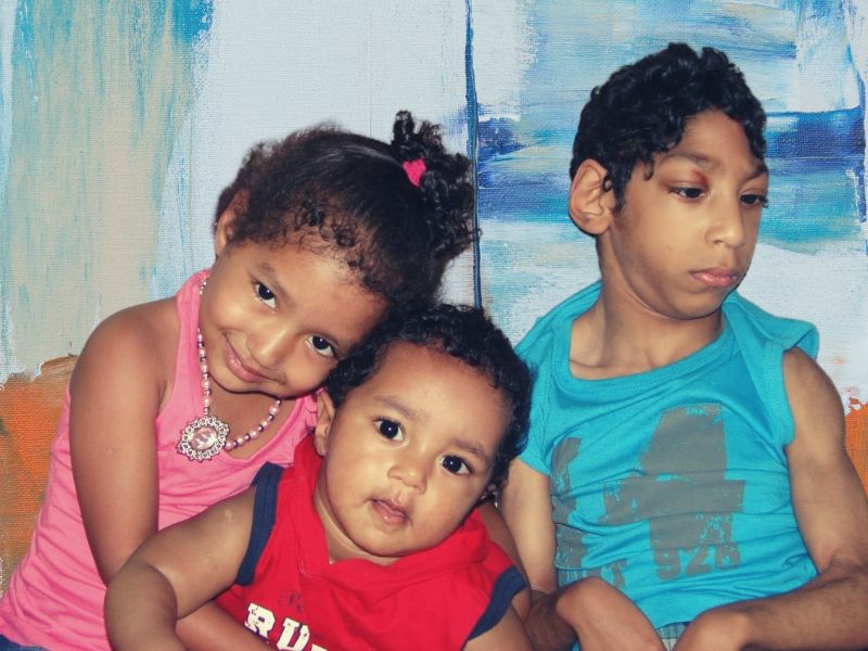 Our 3 children sitting together with an abstract background, posing for a photo.