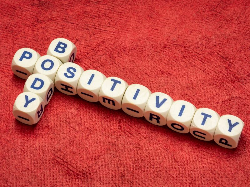 Spelling tiles used to spell out body positivity on a red mat.