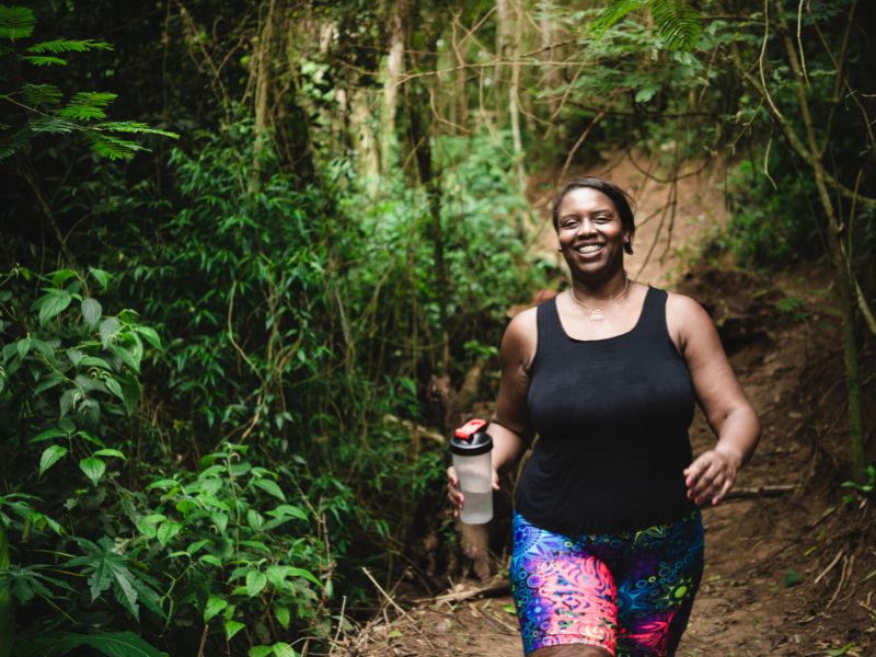 A lady holding a water bottle, while walking through a forest and wearing a colorful tights.