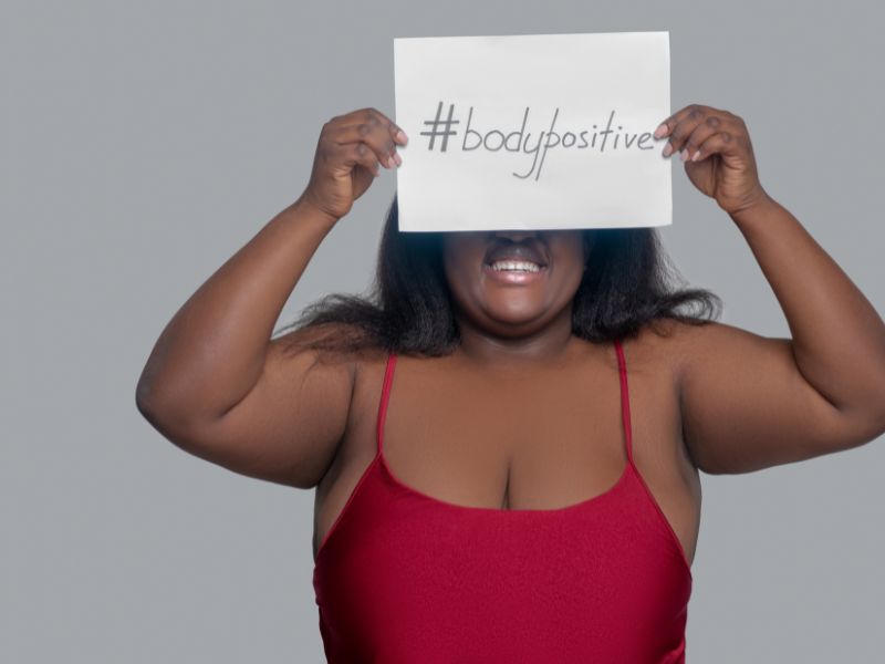 A lady wearing a red top, holding an A4 page with the words, #bodypositive.