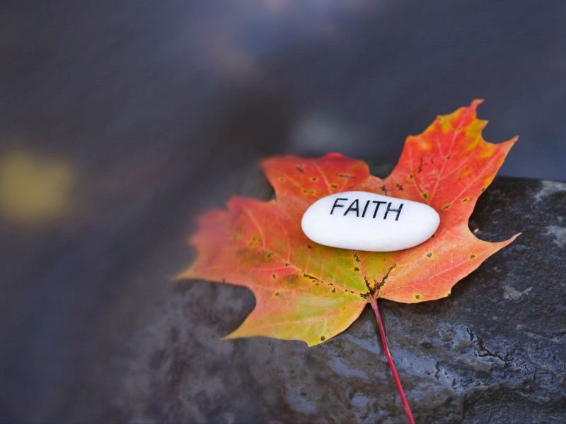 An autumn leaf with a white stone engraved with the word faith on it.