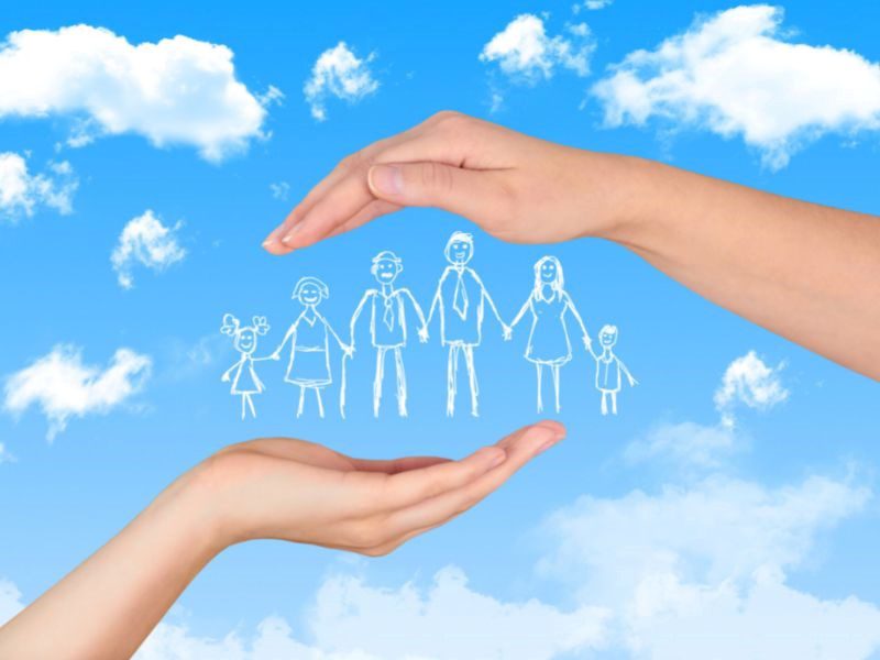 An image of a family: two kids, a husband, a wife and in-laws drawn with white between two hands against a backdrop of a blue sky with fluffy white clouds.