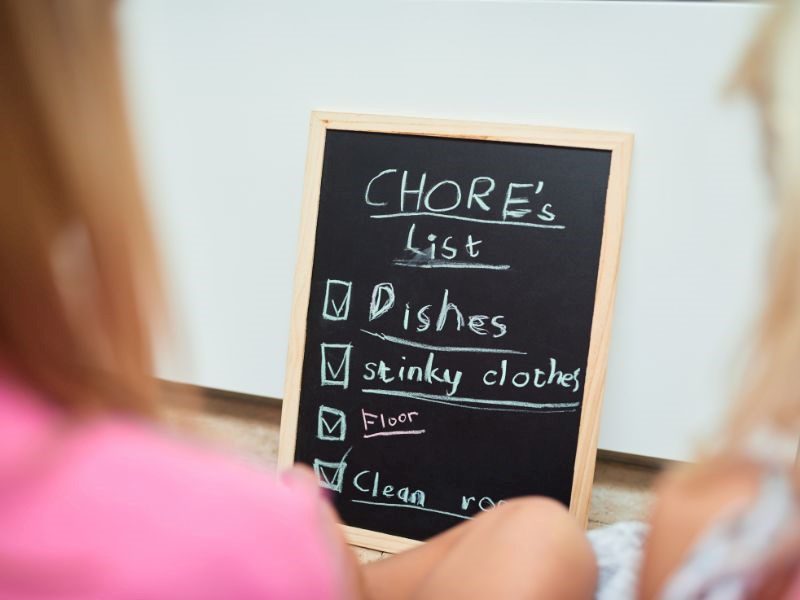A pic of a blurred kid looking at a black chalk board showing chalked list of chores that are completed as they are ticked off.