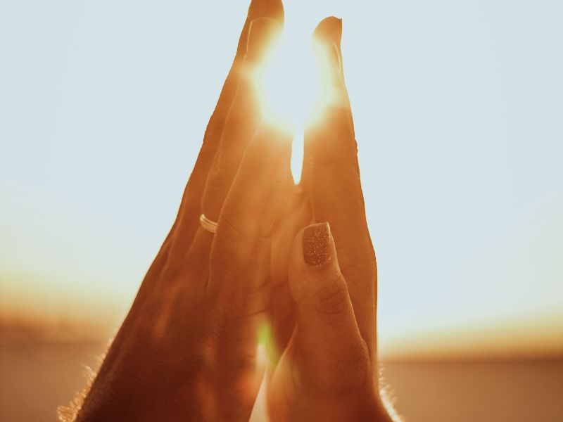 Image depicts the act of learning to communicate with your partner by touching hands, palms facing each other with sunlight shining meaningfully as a backdrop.