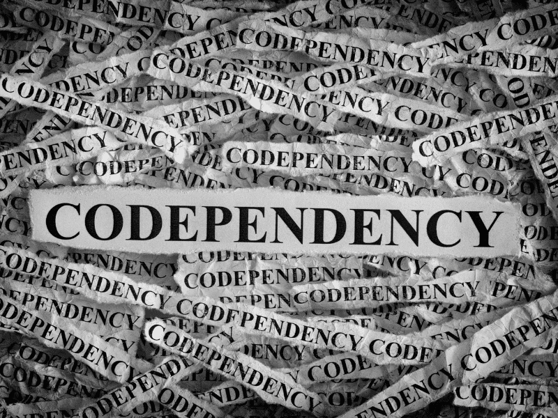 The image shows strips of white paper on top of each other with the word 'codependency' written in bold print