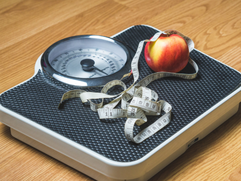 Image shows a floor scale with measuring tape and an apple on top.