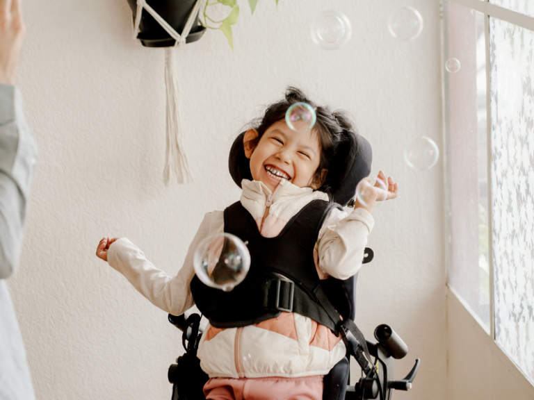 A smiling special needs child strapped into a chair watching bubbles
