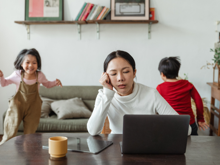 Exhausted mother working at a desk while her children play noisily in the background