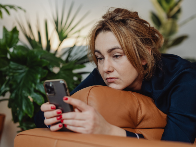 Woman looking at her phone while Laying on a sofa